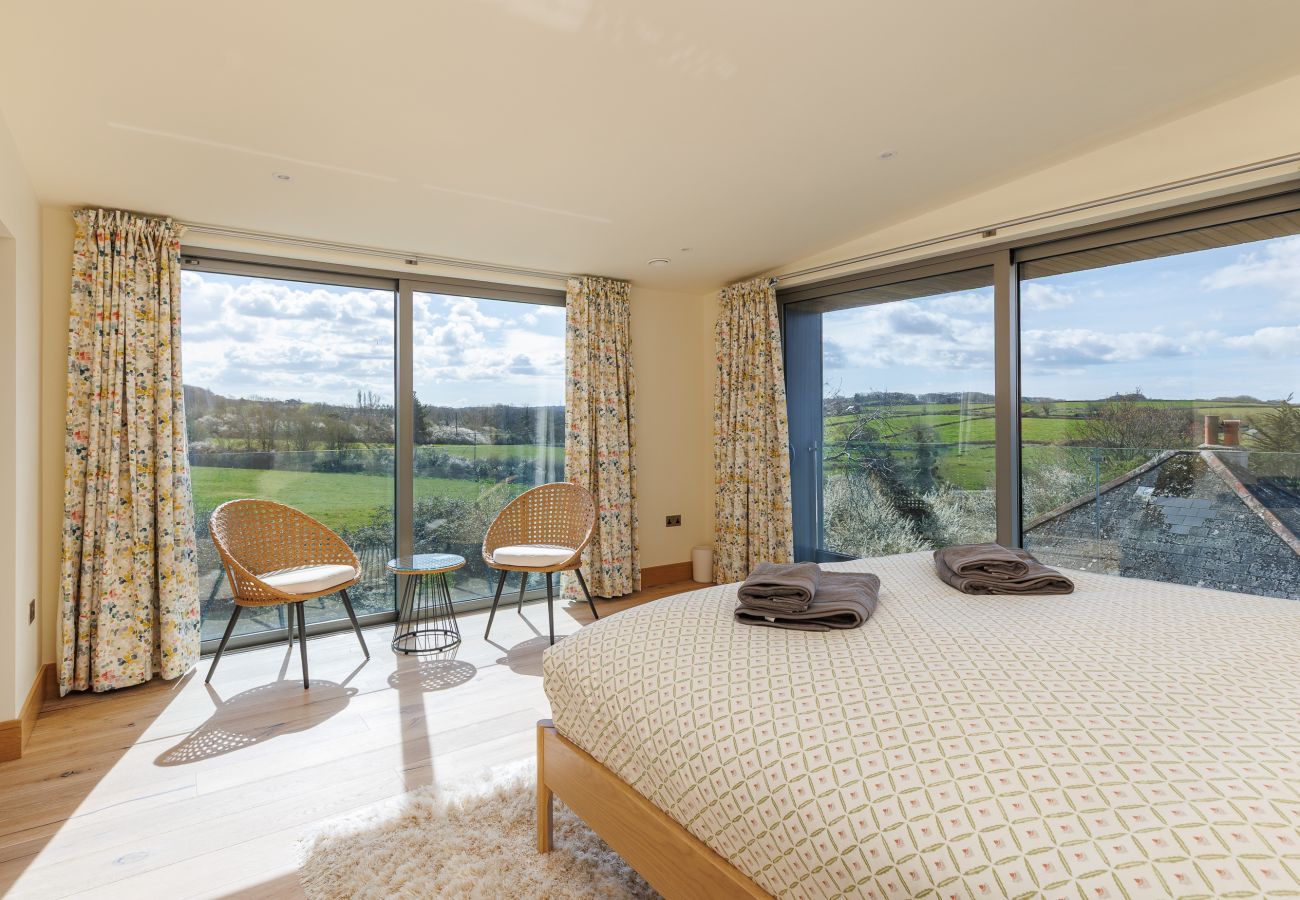 Master bedroom at Rena’s Retreat with double-aspect windows, private balcony, en-suite bathroom, and countryside views with glimpses of the sea