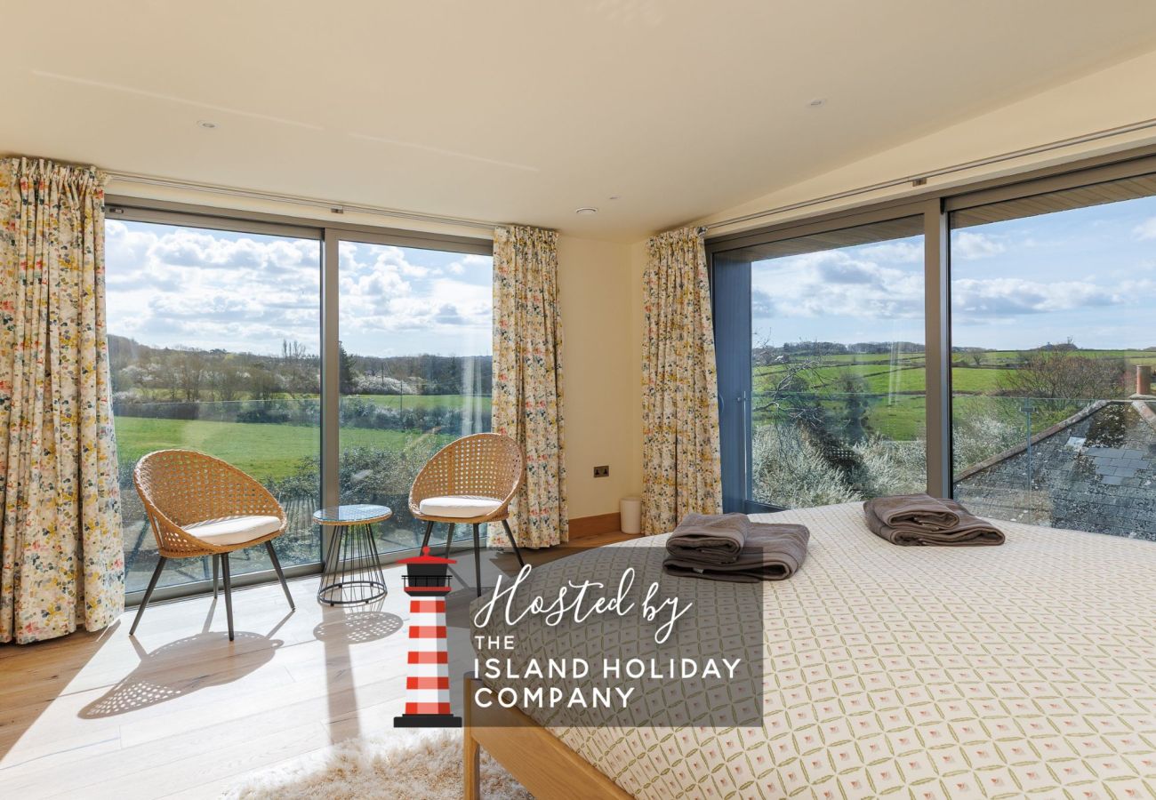 Master bedroom at Rena’s Retreat with double-aspect windows, private balcony, en-suite bathroom, and countryside views with glimpses of the sea