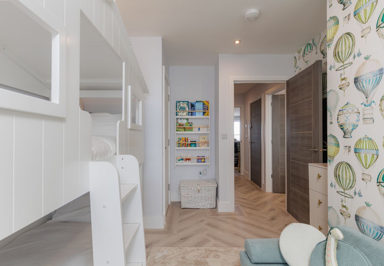 Children’s bedroom with house-style bunk beds, books and colourful balloon wallpaper at Hummingbird, Sandown.